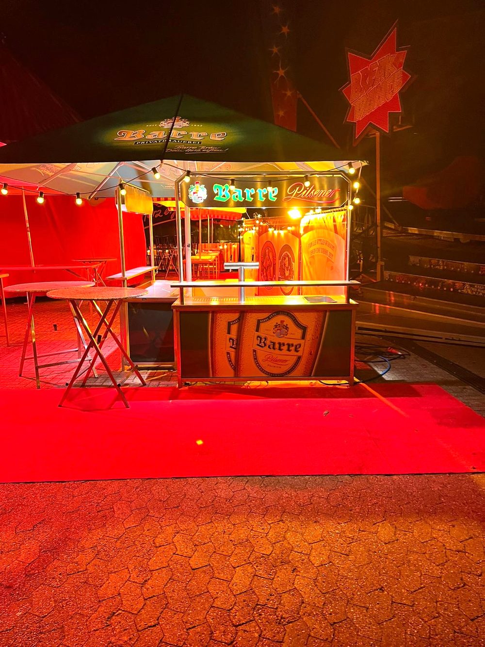 Beleuchtete Theke mit Barre-Pilsener-Motiv bei Nacht